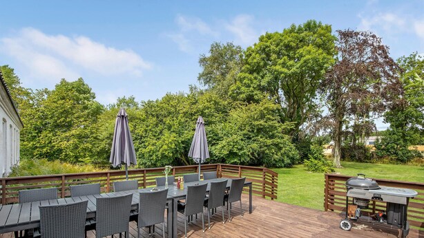 An outdoor deck with a dining area, two umbrellas, and a barbecue grill. - Awesome home in Nexø with sauna (Nexø)