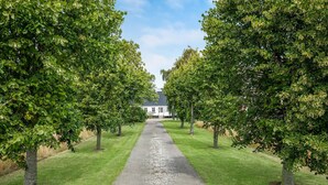 A pathway leading to a white building surrounded by lush green trees. - Awesome home in Nexø with sauna (Nexø)