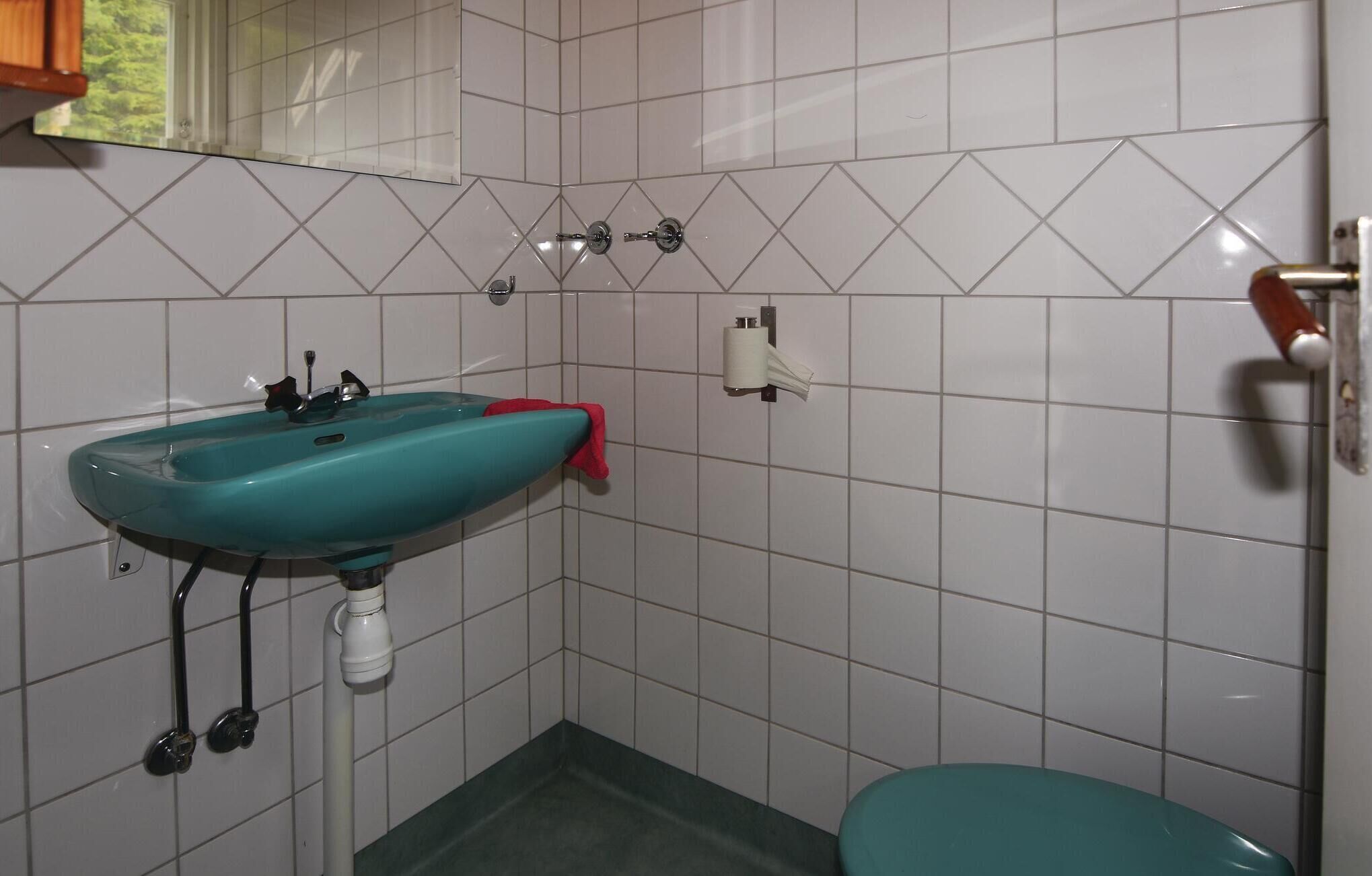 A bathroom with a turquoise sink, white tiles, a toilet, and a mirror.
