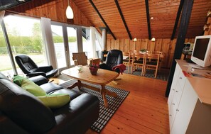 Ein gemütliches Zimmer mit Holzbalkendecke, einer Couch mit Kissen, einem Esstisch mit Stühlen, einem Kamin und einem Fernseher.