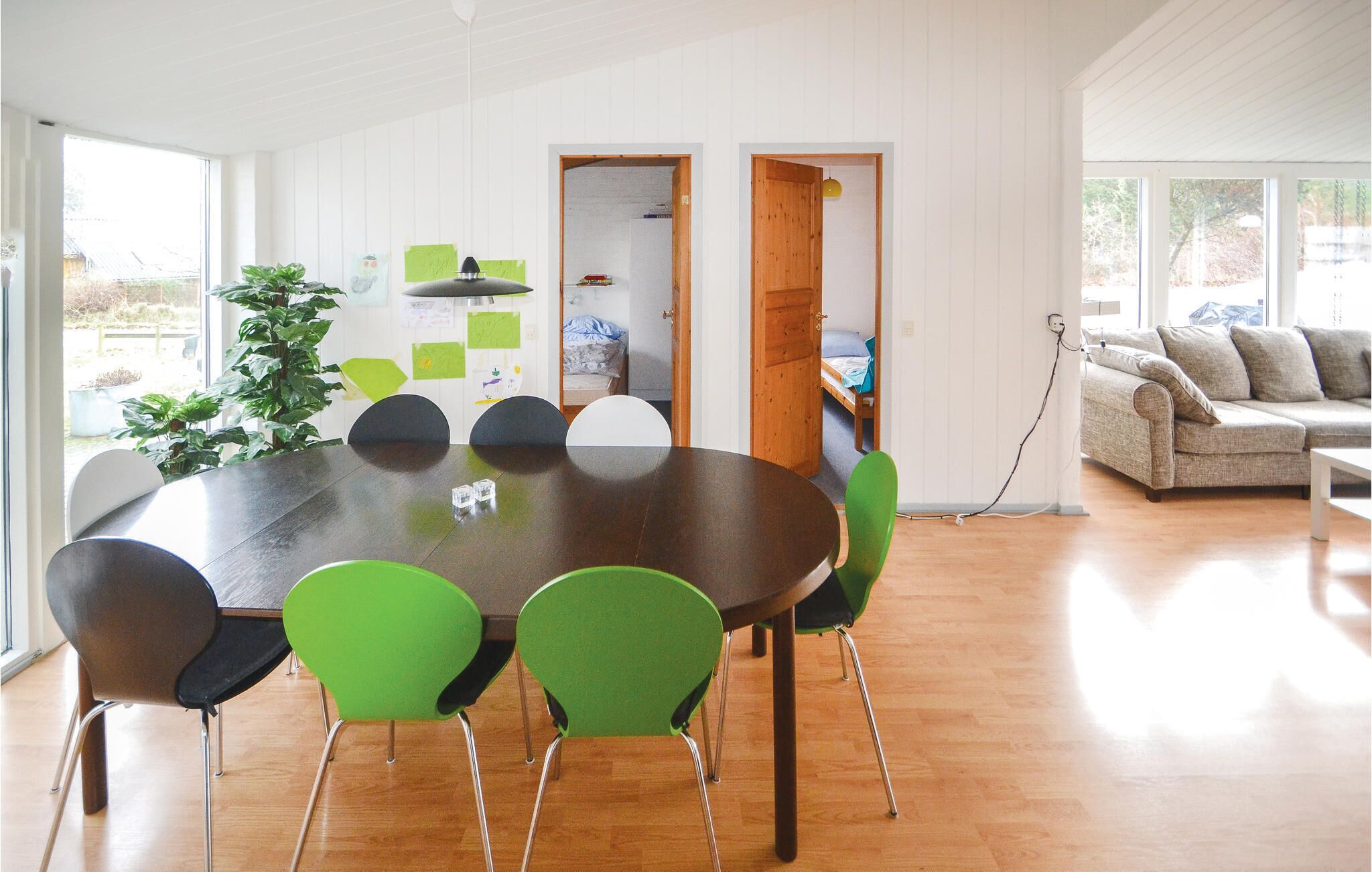 A modern dining area with a round table, green chairs, and a wooden floor.
