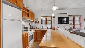 A kitchen with wooden cabinets, a white refrigerator, a stove, a sink, and a television mounted above the counter. - 2 bedroom lovely home in Broager (Broager)