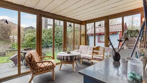 A conservatory with large windows, wicker furniture, a round table, and a view of the garden and neighboring buildings. - 2 bedroom lovely home in Broager (Broager)