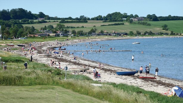 A beach with people swimming and sunbathing, boats, and a grassy area with houses in the background. - 2 bedroom lovely home in Broager (Broager)