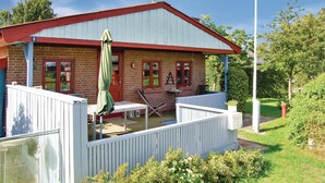 A two-story house with a red roof and white walls, featuring a patio with a table and chairs, a green umbrella, and a fenced garden area. - 2 bedroom lovely home in Broager (Broager)