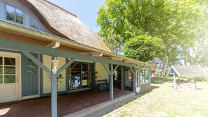 A building with a thatched roof, a covered porch, and a sign indicating 'ZUR HOME.' - Apartment OG - Apartments in thatched house (Ummanz)