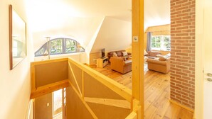 A loft-style room with a wooden staircase, a sofa, a coffee table, and a view of the outdoors. - Apartment OG - Apartments in thatched house (Ummanz)