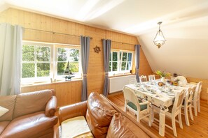 A cozy room with a wooden ceiling, a dining table set for four, and a leather sofa. - Apartment OG - Apartments in thatched house (Ummanz)