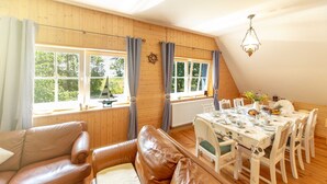 A cozy room with a wooden ceiling, a dining table set for four, and a leather sofa. - Apartment OG - Apartments in thatched house (Ummanz)