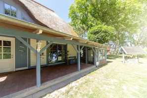 A building with a thatched roof, a covered porch, and a sign indicating 'ZUR HOME.' - Apartment OG - Apartments in thatched house (Ummanz)