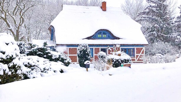 A snow-covered house with a brick exterior, a chimney, and a blue window frame. - Apartment OG - Apartments in thatched house (Ummanz)