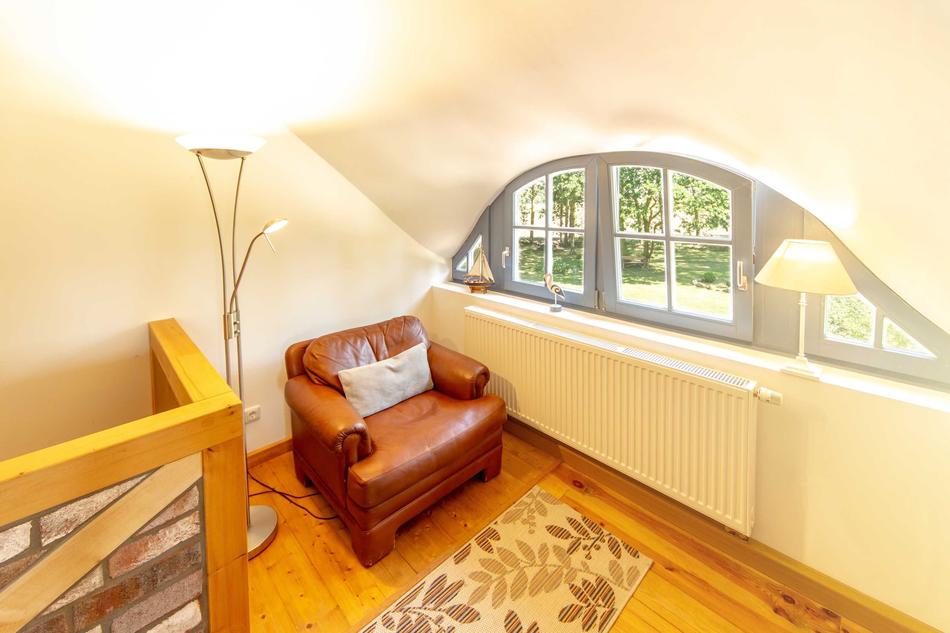 A cozy room with a brown leather sofa, a patterned rug, a radiator, and a window with a view of greenery.
