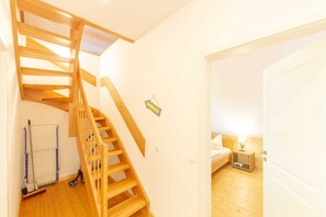 A wooden staircase leading to a bedroom with a bed, bedside table, and a lamp. - Apartment OG - Apartments in thatched house (Ummanz)