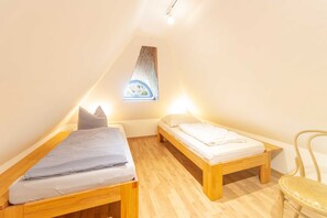 A small, well-lit room with two wooden beds, a single chair, and a sloped ceiling with a skylight.
