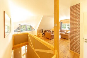 A loft-style room with a wooden staircase, a sofa, a coffee table, and a view of the outdoors. - Apartment OG - Apartments in thatched house (Ummanz)