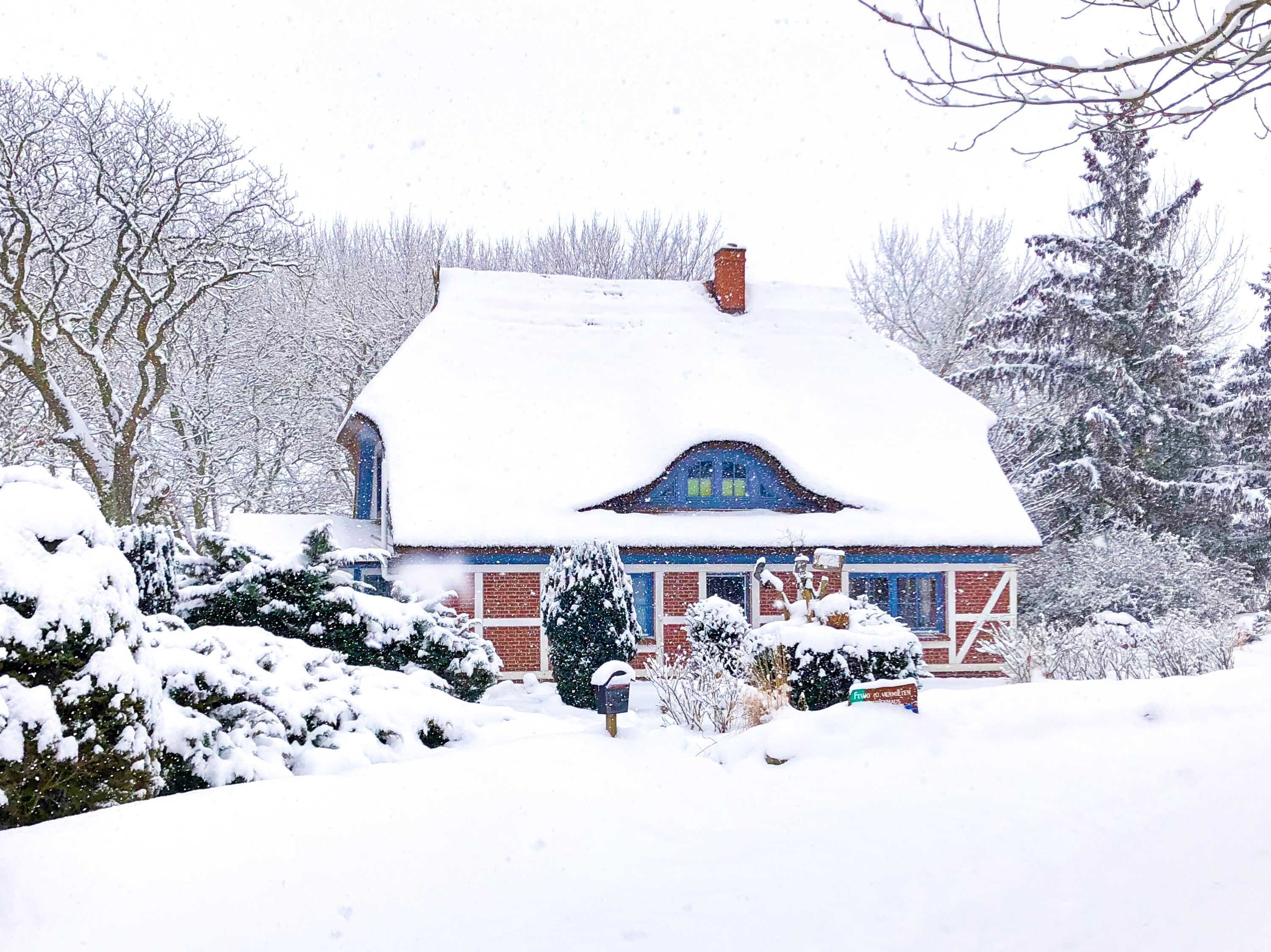 A snow-covered house with a brick exterior, a chimney, and a blue window frame.