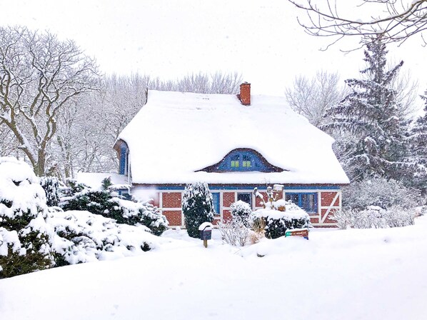 A snow-covered house with a brick exterior, a chimney, and a blue window frame. - Apartment OG - Apartments in thatched house (Ummanz)