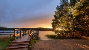 A wooden pier leading to a sandy beach with a lake and trees in the background.