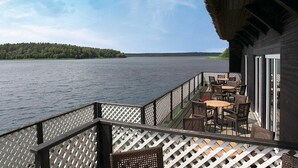 A deck with outdoor seating overlooking a lake, a thatched roof structure, and a forested island in the distance.