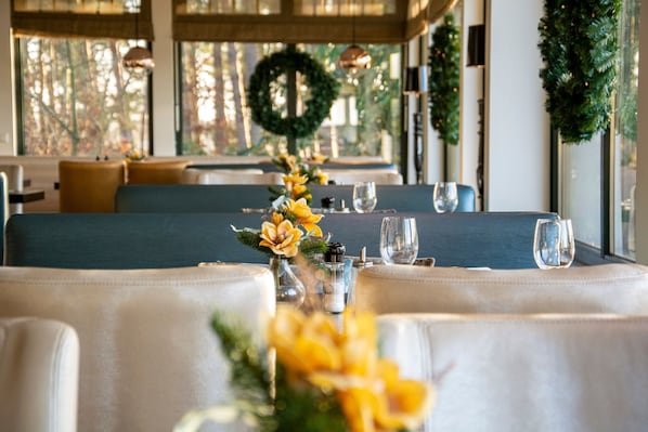 Un restaurant avec une longue table dressée pour le dîner, agrémentée d’un centre de table décoratif et d’une guirlande accrochée au mur.