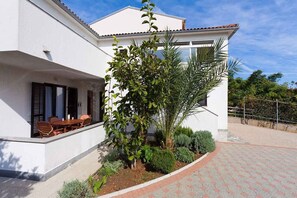 Una casa moderna con patio, zona pranzo e giardino con diverse piante.