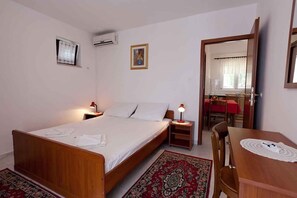 Una camera da letto con un letto singolo, comodini, una sedia di legno, un tavolino, uno specchio e una finestra con tende.