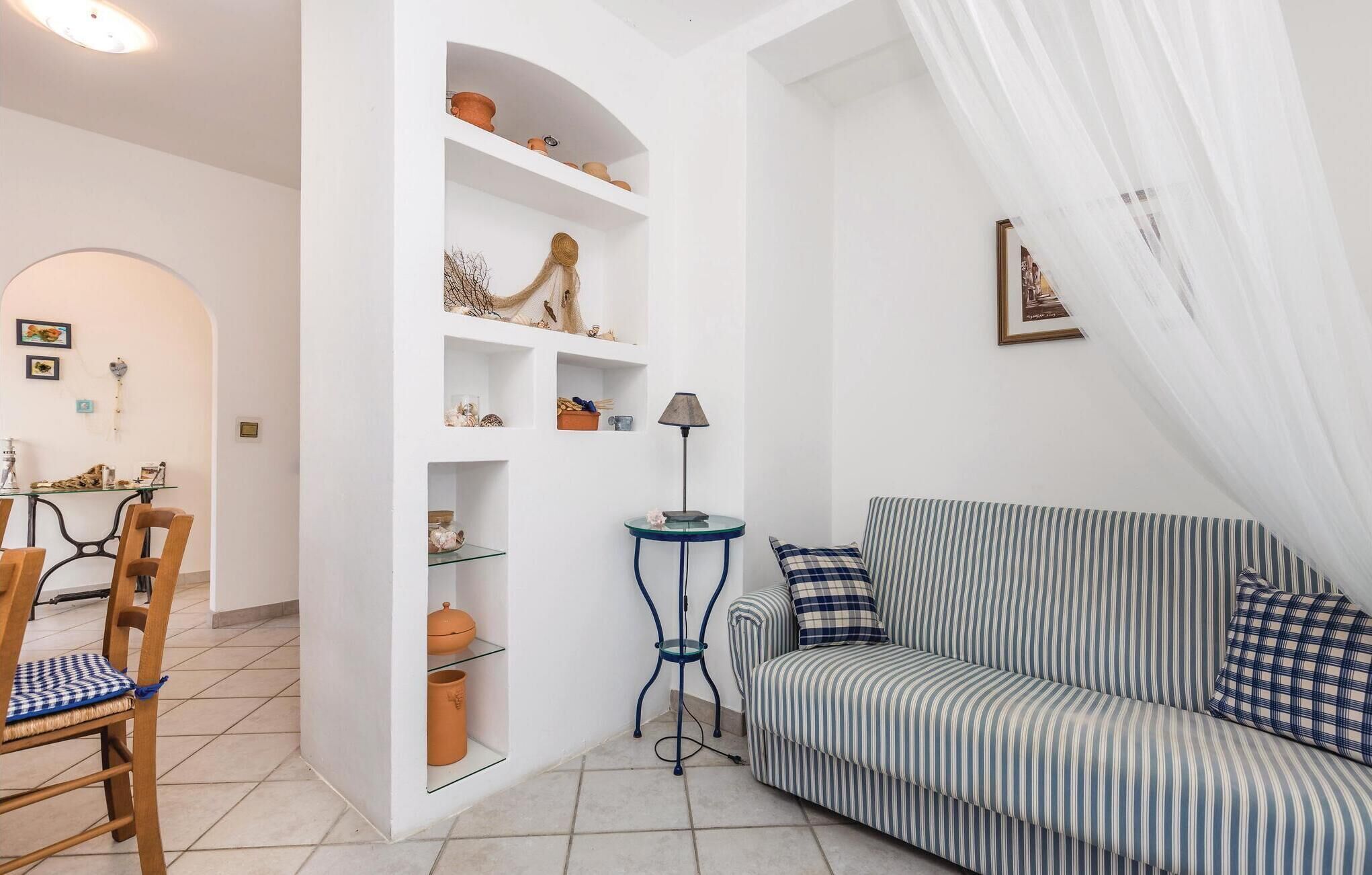 A living room with a striped sofa, a small table with a lamp, and shelves with decorative items.