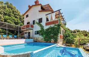 Relax by the mosaic tile pool surrounded by lush greenery and a traditional facade with red accents.