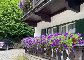 A building with a balcony, a stone wall, and a car parked in front. - DZ Standard double room for single use - Bio Design Boutique Hotel Landhaus St. (Bad Wiessee)