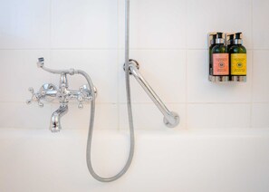 Une salle de bain équipée d’un système de douche chromé, d’un pommeau de douche à main et de deux flacons de produits de toilette fixés au mur.