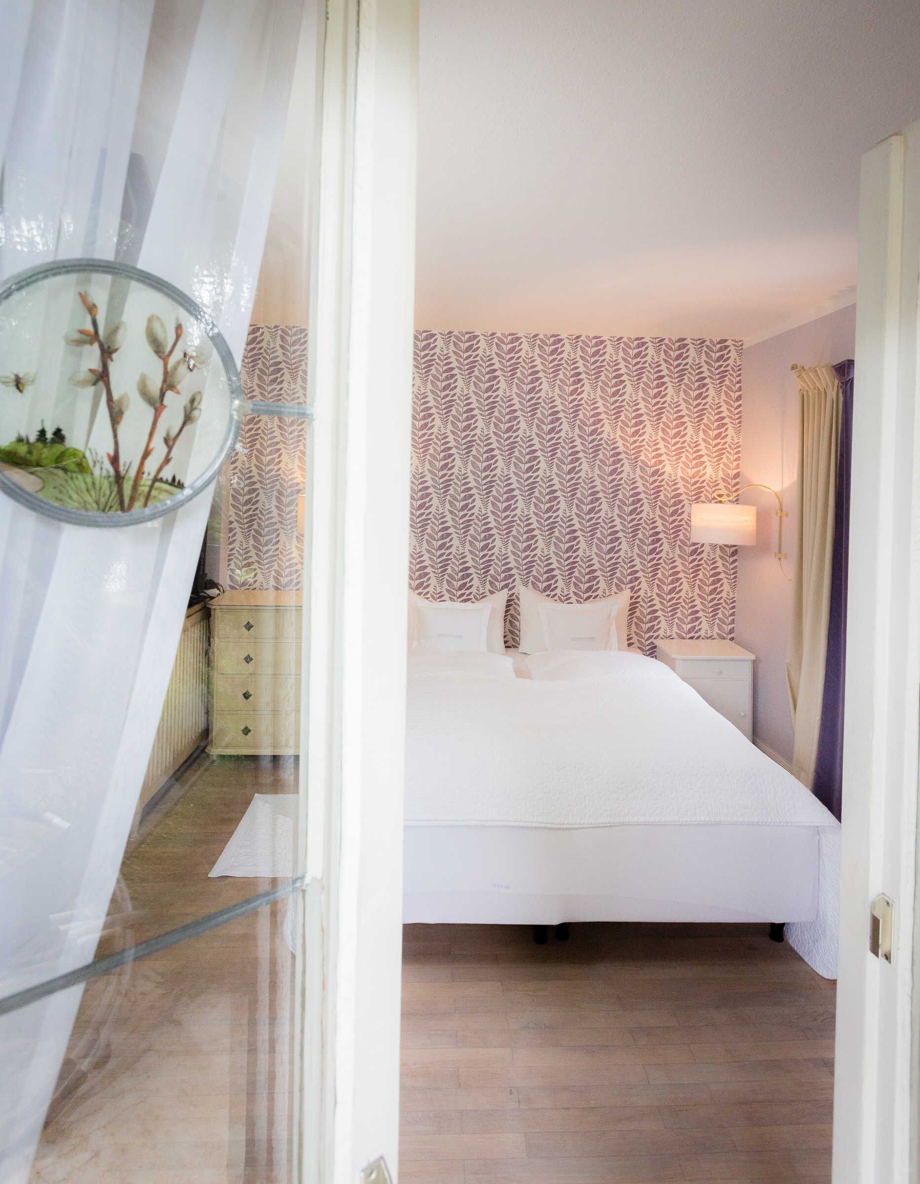 A bedroom with a bed, a nightstand, a lamp, and a patterned wallpaper.