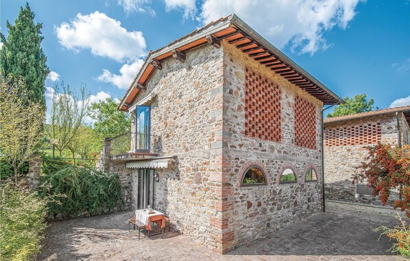 Un bâtiment en pierre avec un toit en tuiles, un petit balcon et une table avec des chaises à l’extérieur.