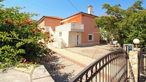 A two-story house with a balcony, a paved patio, and a metal fence. - Holiday apartment mit Klimaanlage und Terrasse (Šilo)