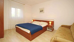 A bedroom with a wooden bed, a bedside table with a lamp, a sofa, and a window with curtains. - Holiday apartment mit Klimaanlage und Terrasse (Šilo)