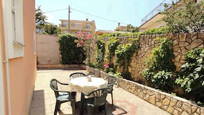 An outdoor patio with a round table and four chairs, surrounded by a stone wall and lush greenery. - Holiday apartment mit Klimaanlage und Terrasse (Šilo)