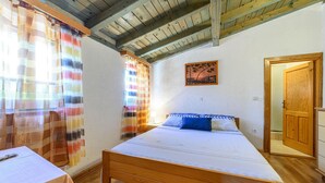 A bedroom with a wooden bed, a nightstand, a table with a white tablecloth, and a door. - 1 bedroom awesome home in Jadrija (Jadrija)