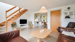 Uma sala de estar moderna com escada de madeira, televisão, espaço para refeições e cozinha.