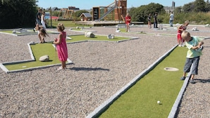 Ein Spielbereich für Kinder mit Minigolfanlage, einer Holzspielkonstruktion und einem kleinen Gebäude im Hintergrund.