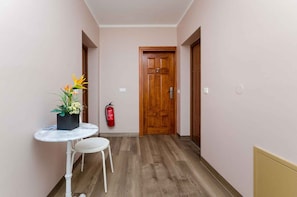 Um corredor estreito com uma porta de madeira, uma pequena mesa com uma cadeira e um vaso com planta.