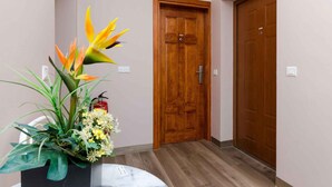 A hallway with a wooden door, a potted plant with yellow flowers, and a fire extinguisher on the wall.