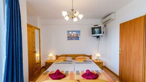 A bedroom with a wooden bed, two bedside tables with lamps, a TV on the wall, and a painting above the bed.