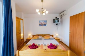 Um quarto com cama de madeira, duas mesas de cabeceira com abajures, uma TV na parede e um quadro sobre a cama.