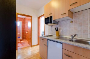 Cozinha com armários de madeira, pia de aço inoxidável e micro-ondas.
