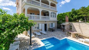 A multi-story building with a pool, outdoor seating, and a stone wall.