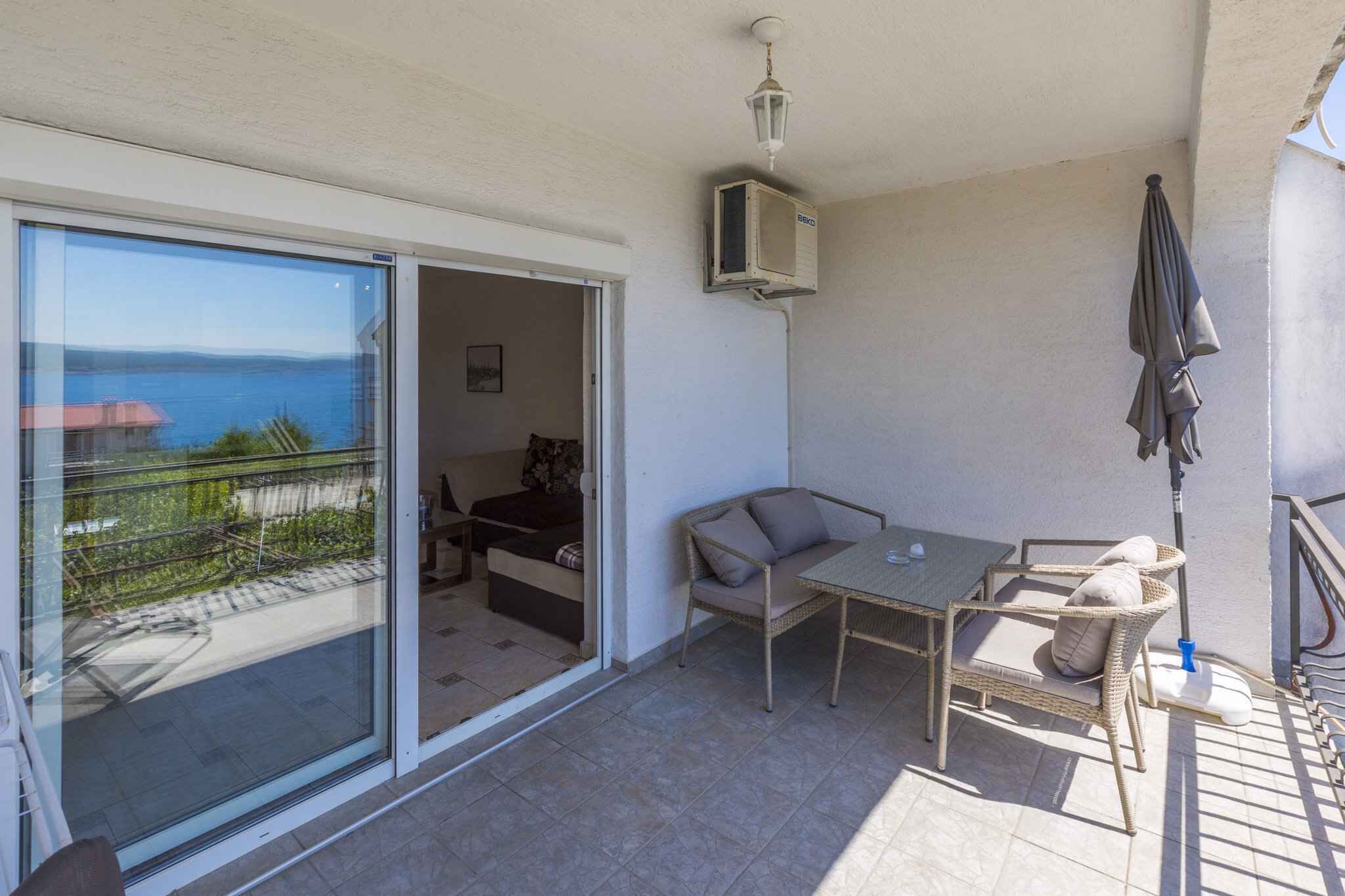 A balcony with a table and chairs, a sliding glass door, and a view of the sea.