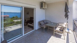 Un balcón con mesa y sillas, una puerta corredera de vidrio y vista al mar.