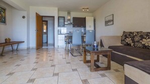 Una sala de estar con sofá, una mesa de centro y un comedor con sillas y una mesa. Se ve una cocina al fondo.