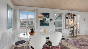 Spisestue med et rundt bord, hvide stole, træloft og udsigt til bygninger gennem store vinduer.