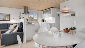 Et moderne køkken med hvide skabe, et spiseområde med et rundt bord og en grå sofa.