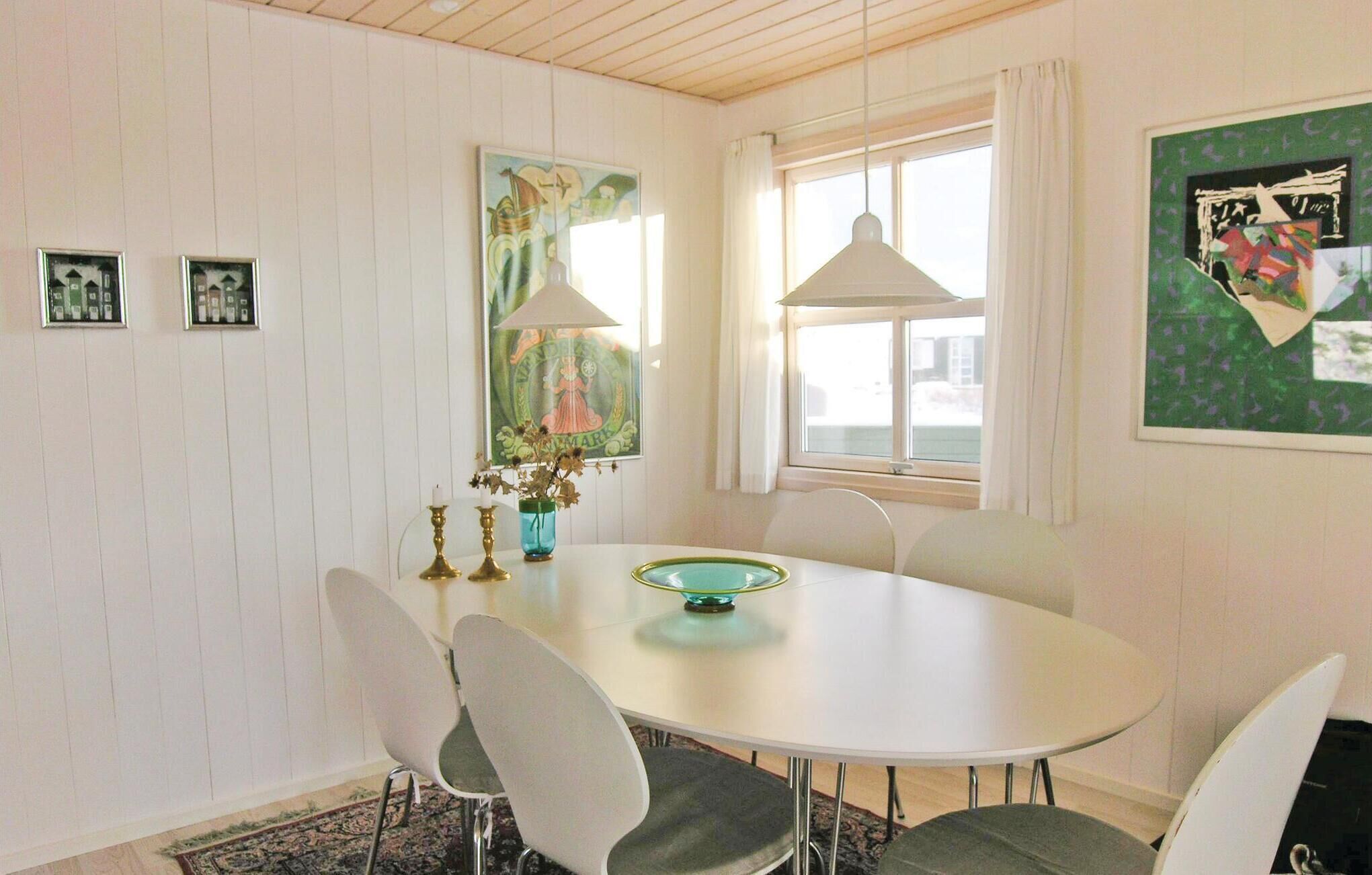 A dining area with a round table, four chairs, two wall-mounted lamps, and framed artwork.